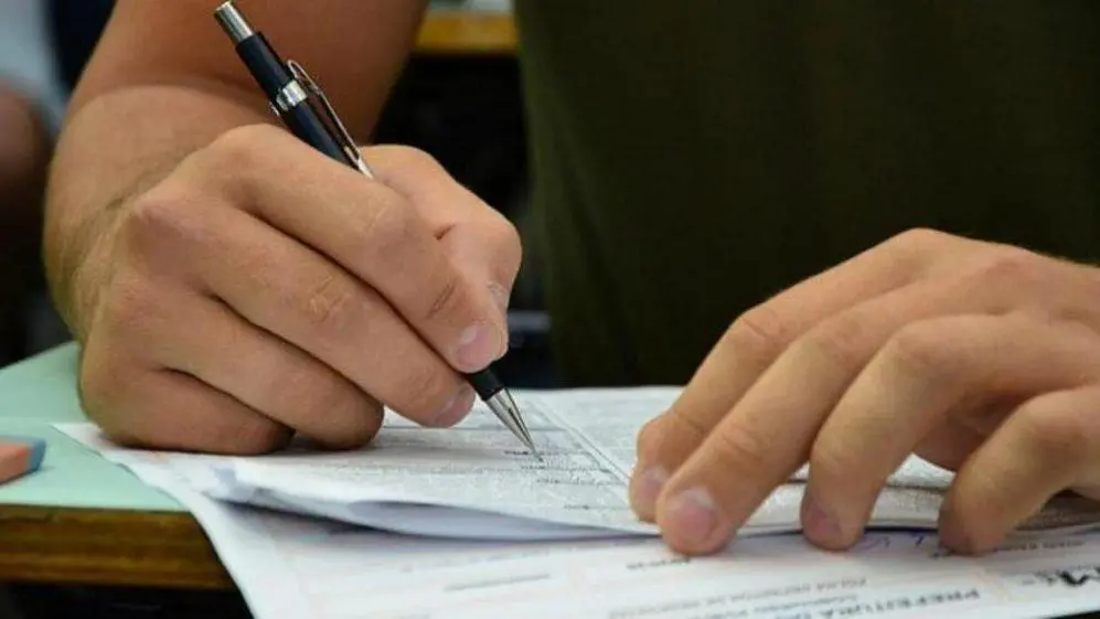 A imagem mostra um homem realizando uma prova do Enem. É possível ver as mãos dele, a caneta e o caderno de provas.