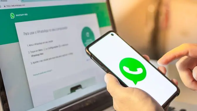 pessoa segurando celular na mao mostrando aplicativo whatsapp e tambem vendo o aplicativo whatsapp web na tela do computador.