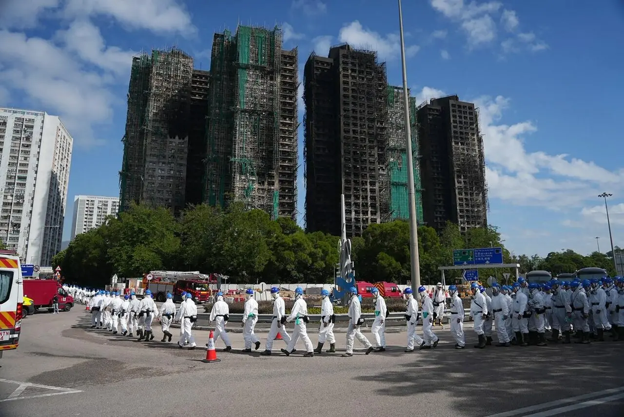 Imagem de quatro prédios incendiados com grupo de voluntários vestidos de branco na frente, formando uma fila.