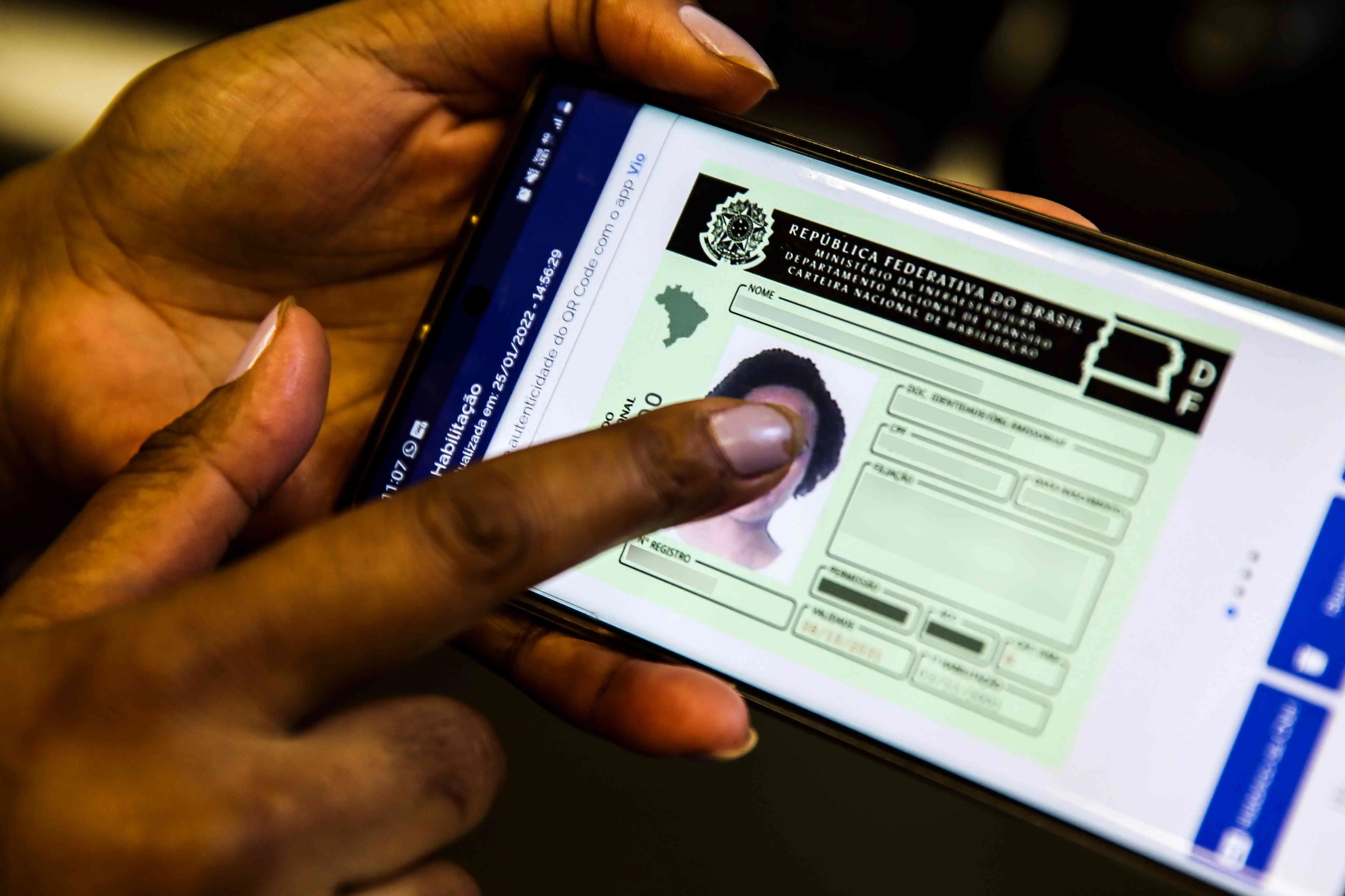 Mãos segurando um smartphone com a Carteira Nacional de Habilitação (CNH) Digital exibida na tela.
