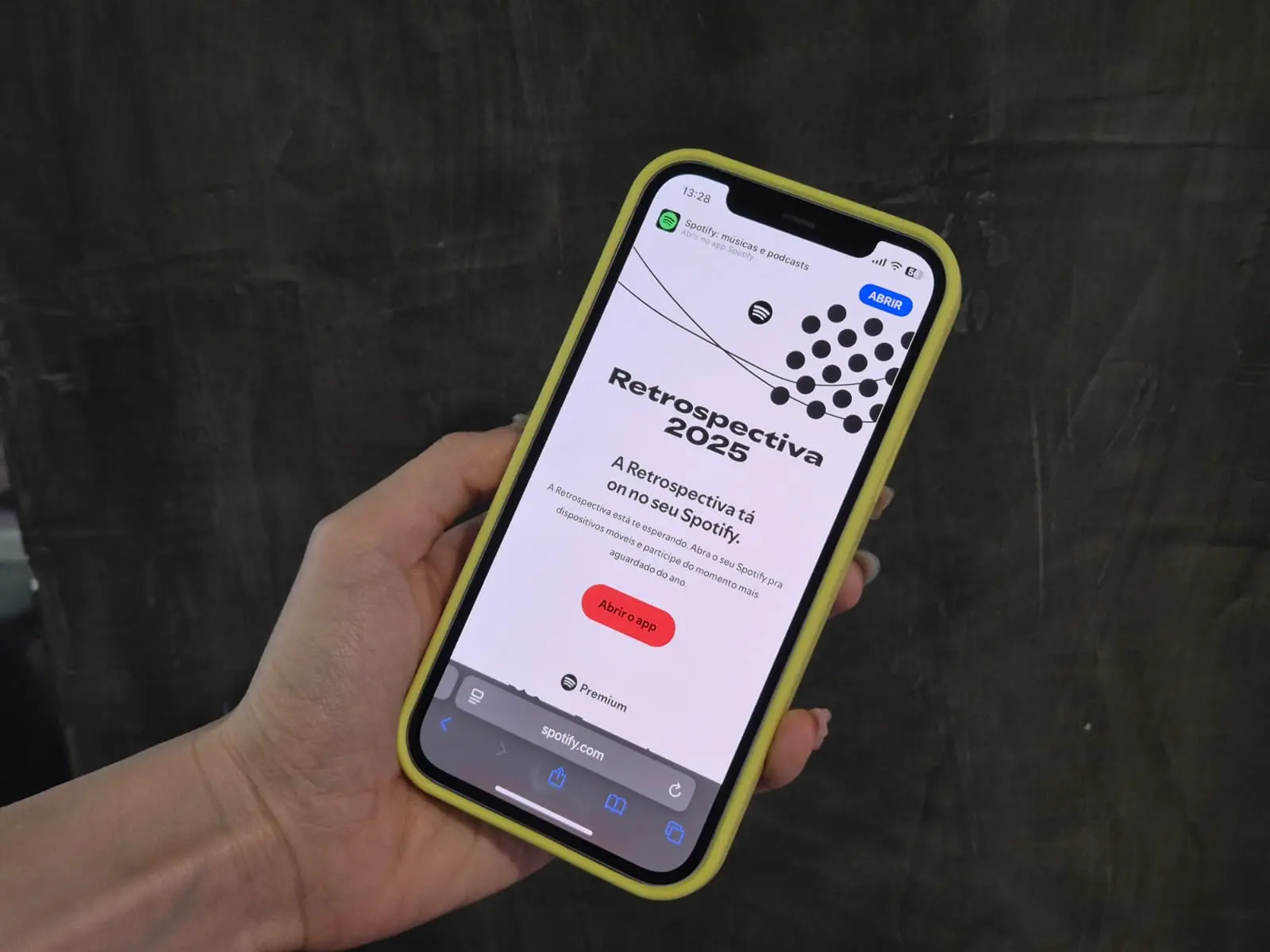 Mão segurando um iPhone com capa amarela exibindo a tela Retrospectiva Wrapped 2025 do Spotify.