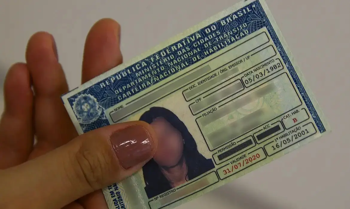 Imagem mostra close-up da Carteira Nacional de Habilitação (CNH) mostrando informações e a foto borrada do condutor.