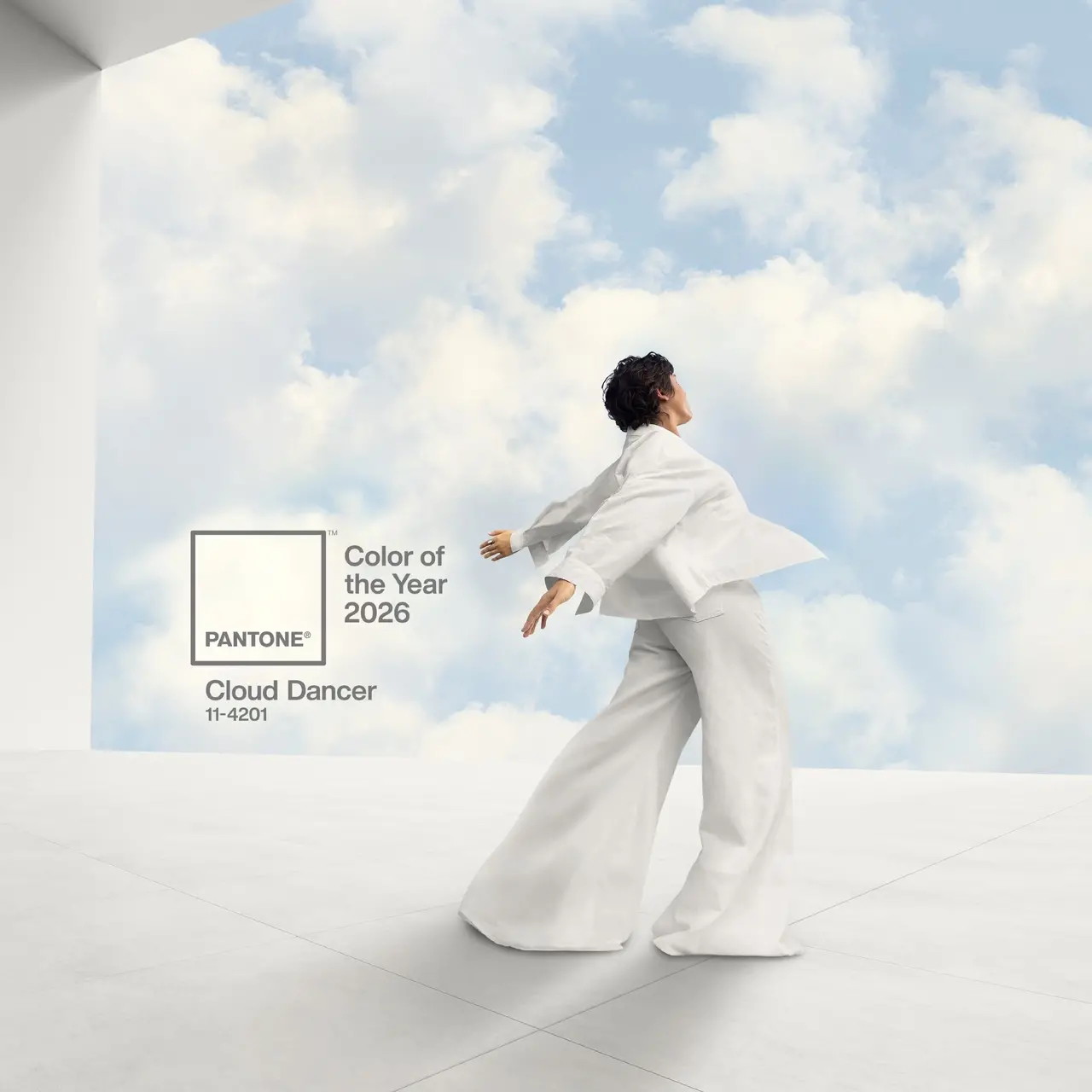 Foto de divulgação da cor do ano de 2026 da Pantone. Uma pessoa de branco, dançando ou posando em frente a uma parede de fundo com um céu azul e nuvens brancas.