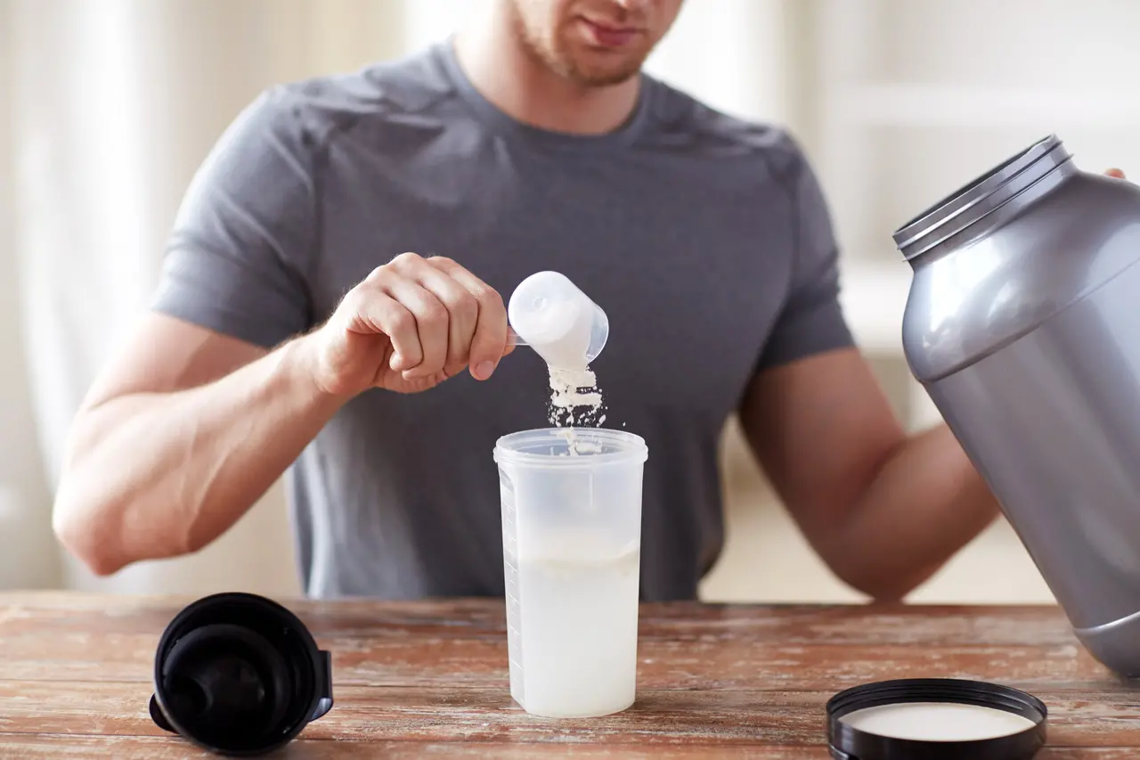 Homem colocando scoop de whey em garrada