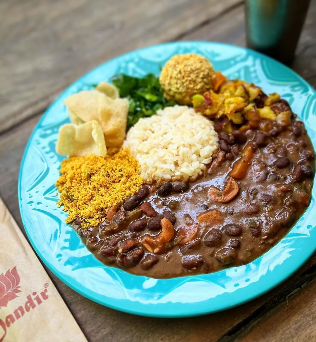 No Mandir.amor, a feijoada Mandiresca é composta de legumes selecionados, farofinha crocante, couve manteiga no azeite de oliva, torresmo vegetal e sabji; sem glúten e sem soja
