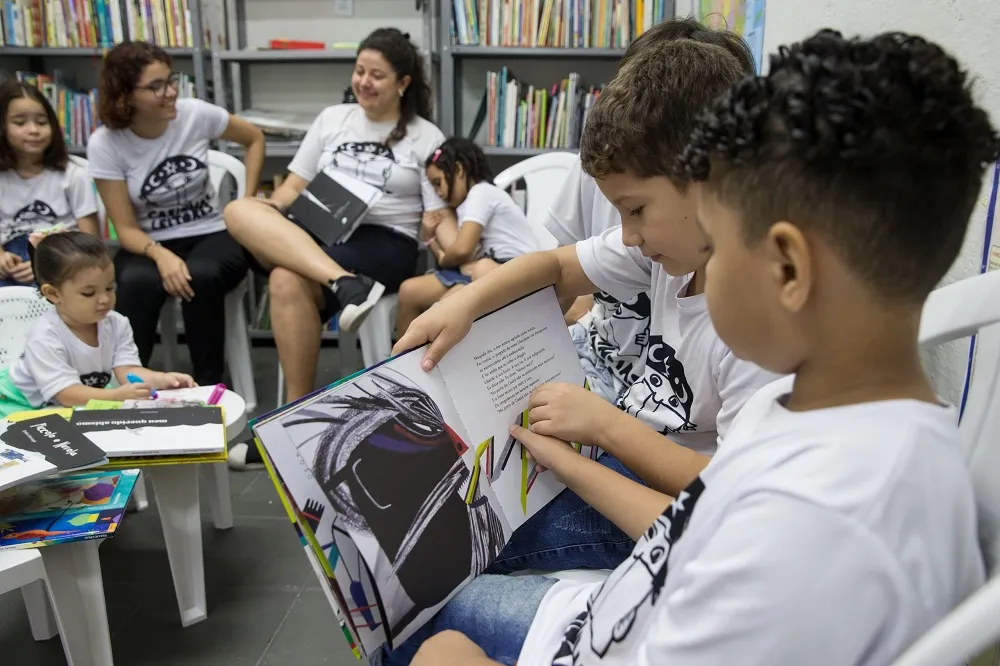 Uma criança ajuda a outra a ler na biblioteca dos Cabinhas