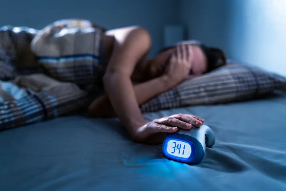 pessoa com insônia deitada na cama com despertador na mão