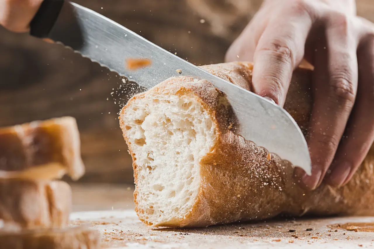 Imagem mostra foco em pão caseiro sendo cortando por uma faca.