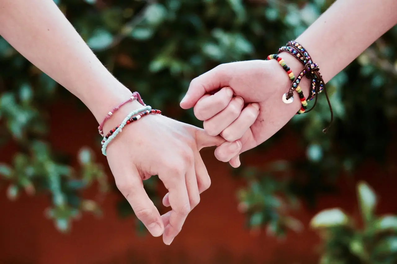 Duas mãos dadas, com pulseiras nos braços