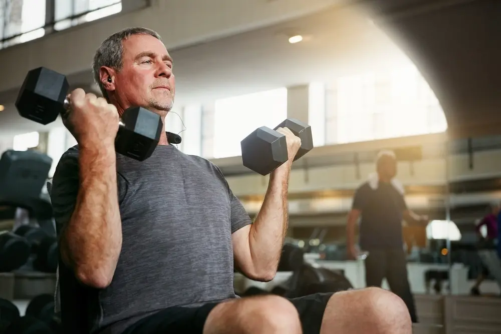 foto de idoso praticando musculação levantando dois alteres em academia