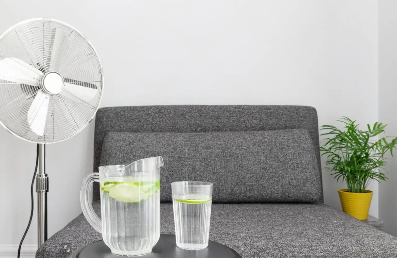 Ventilador de coluna numa sala com sofá e uma mesa de centro com copos de água com limão